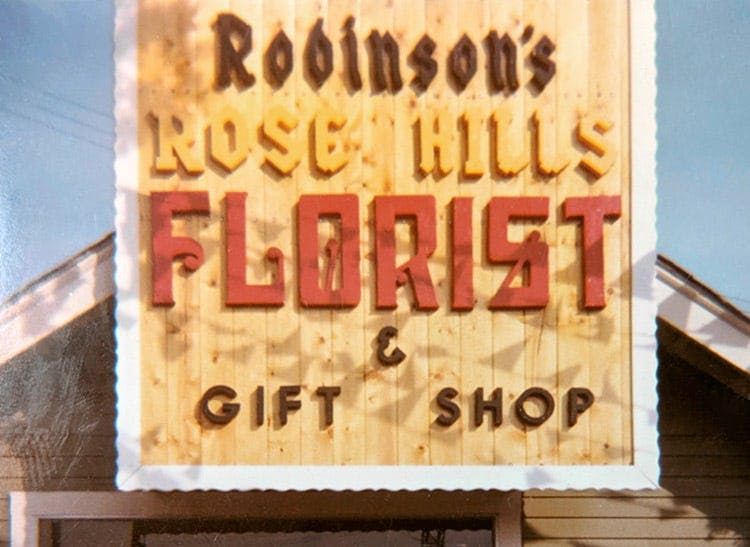 A wooden sign promotes Robinson's Rose Hills Florist and Gift Shop